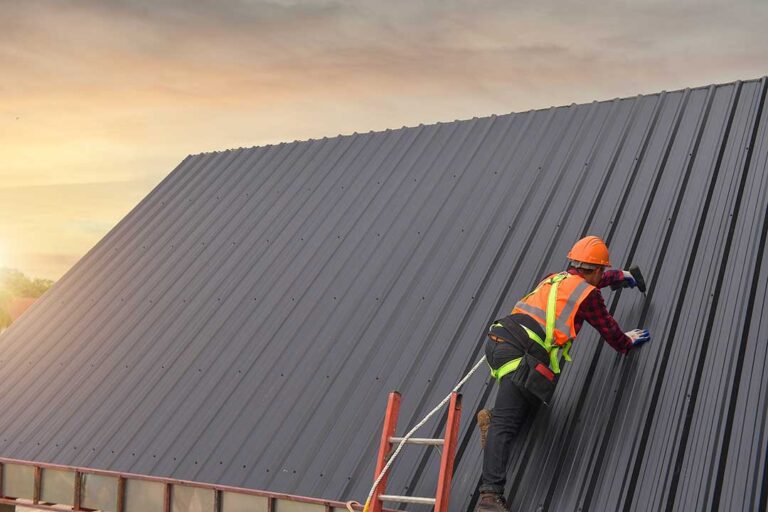 Person inspecting curled shingles and rusted metal roofing from the ground near a residential attic.